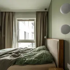 Małe sypialnie inspiracje: przytulne łóżko z zieloną pościelą, zasłony, okno i nowoczesne lampy ścienne.