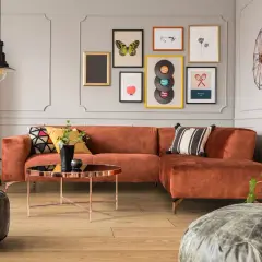 Pomarańczowa kanapa i stolik kawowy tworzą przytulny kącik w stylu mid century modern. Obrazy z płytami winylowymi i motylami dodają charakteru.
