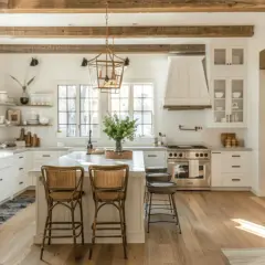 Jasna kuchnia w stylu farmhouse z drewnianymi belkami, wyspą i rattanowymi hokerami.