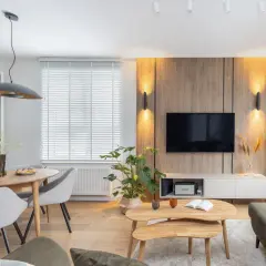 Przytulny salon inspiracje: drewniana ściana z TV, okrągły stół z szarymi krzesłami, stoliki kawowe i rośliny tworzą ciepłą atmosferę.