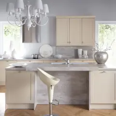 Jasna kuchnia w stylu shabby chic z kremowymi frontami, kamiennym blatem i ozdobnym żyrandolem.