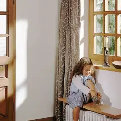 Dziewczynka w sieni zakłada buty. Obok okno z widokiem na ogród i drzwi z ozdobnymi okuciami.
