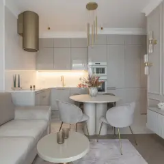Elegancka, mała kuchnia z salonem. Jasna kanapa, okrągły stół z krzesłami i nowoczesna zabudowa kuchenna tworzą przytulną przestrzeń.