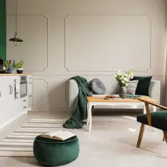 Eleganckie wnętrze w odcieniach butelkowej zieleni i beżu. Kanapa, fotel i puf tworzą przytulną przestrzeń.