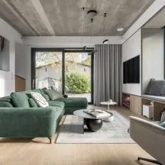 Nowoczesny salon w skandynawskim stylu domu z zieloną sofą, betonowym sufitem i dużym oknem.