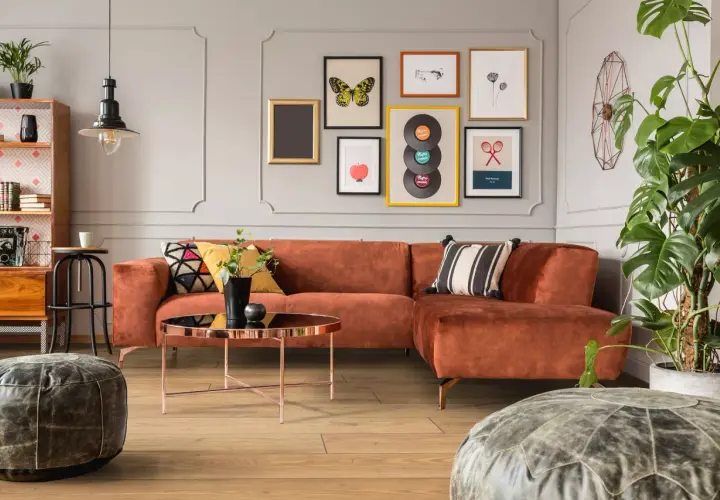 Pomarańczowa kanapa i stolik kawowy tworzą przytulny kącik w stylu mid century modern. Obrazy z płytami winylowymi i motylami dodają charakteru.