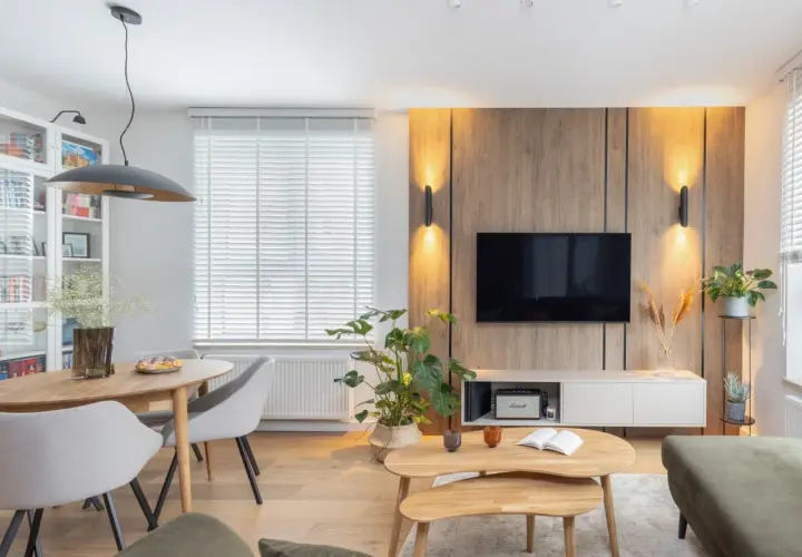 Przytulny salon inspiracje: drewniana ściana z TV, okrągły stół z szarymi krzesłami, stoliki kawowe i rośliny tworzą ciepłą atmosferę.