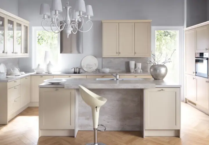 Jasna kuchnia w stylu shabby chic z kremowymi frontami, kamiennym blatem i ozdobnym żyrandolem.