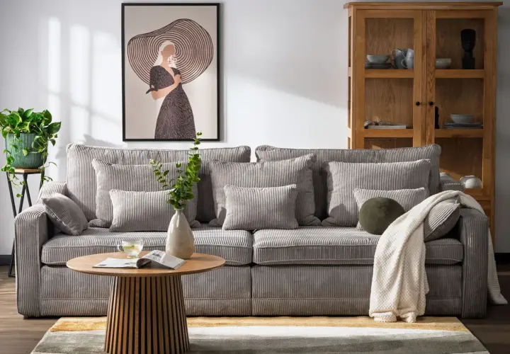 Miękka, sztruksowa kanapa a sofa w salonie, z poduszkami i kocem, obok stolika kawowego i obrazu.