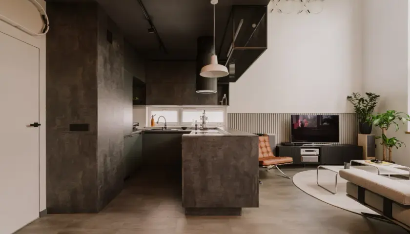 Nowoczesna kuchnia i salon w stylu eco brutalism. Betonowe powierzchnie, ciemne akcenty i minimalistyczne meble tworzą surowy, ale przytulny klimat.