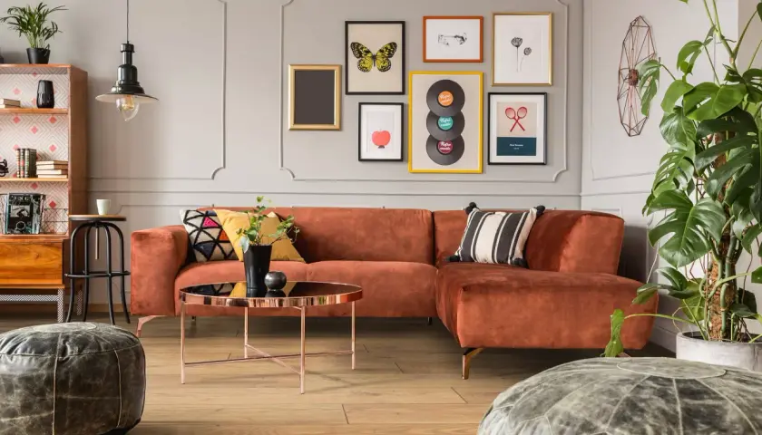 Pomarańczowa kanapa i stolik kawowy tworzą przytulny kącik w stylu mid century modern. Obrazy z płytami winylowymi i motylami dodają charakteru.