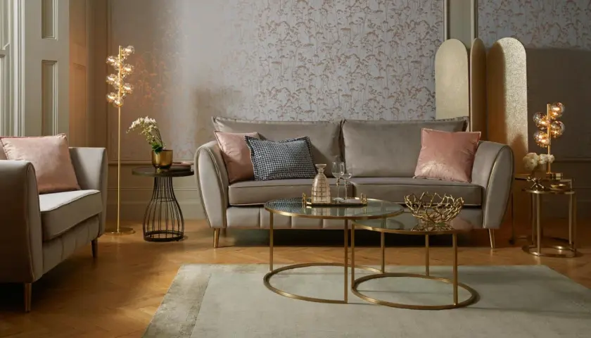 Przytulny salon glamour z beżową sofą, różowymi poduszkami i złotymi dodatkami.