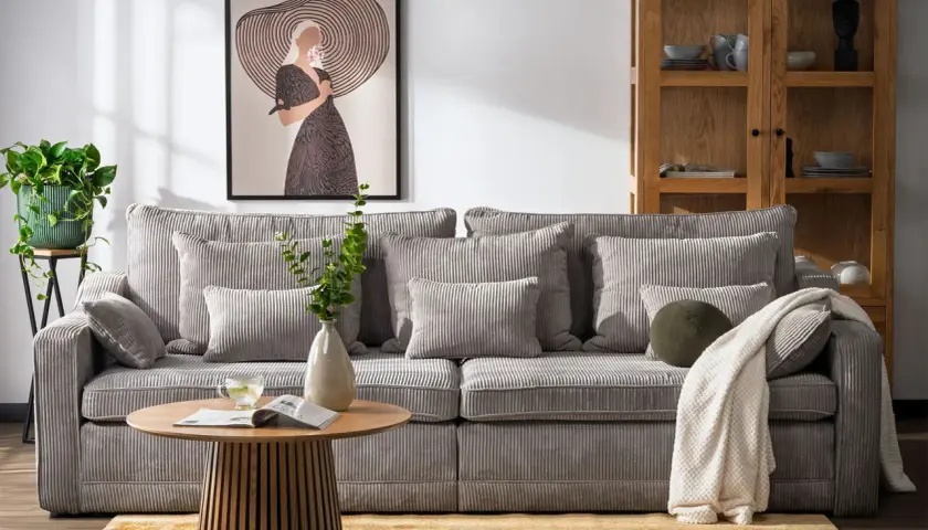 Miękka, sztruksowa kanapa a sofa w salonie, z poduszkami i kocem, obok stolika kawowego i obrazu.