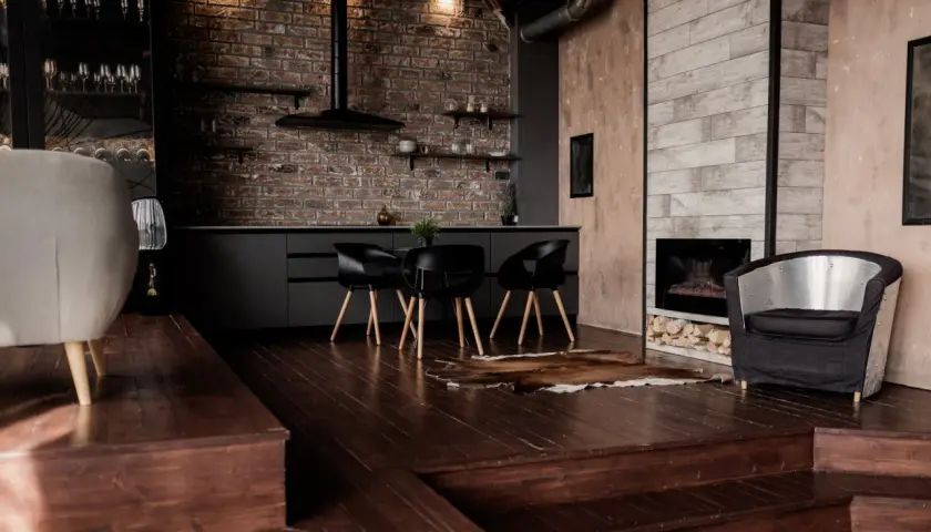 Nowoczesny salon z ciemną podłogą, ceglaną ścianą i designerskimi meblami.