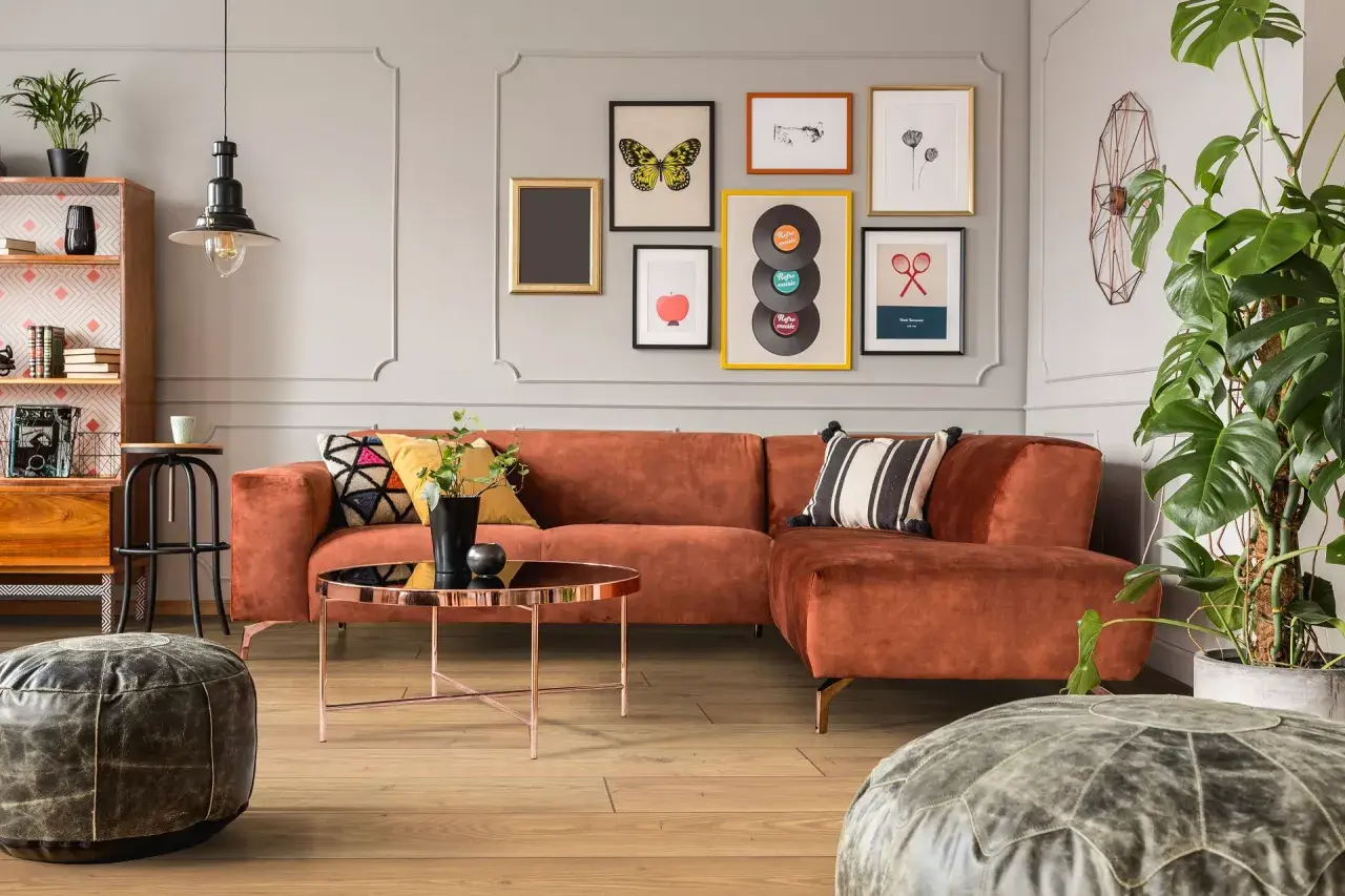 Pomarańczowa kanapa i stolik kawowy tworzą przytulny kącik w stylu mid century modern. Obrazy z płytami winylowymi i motylami dodają charakteru.