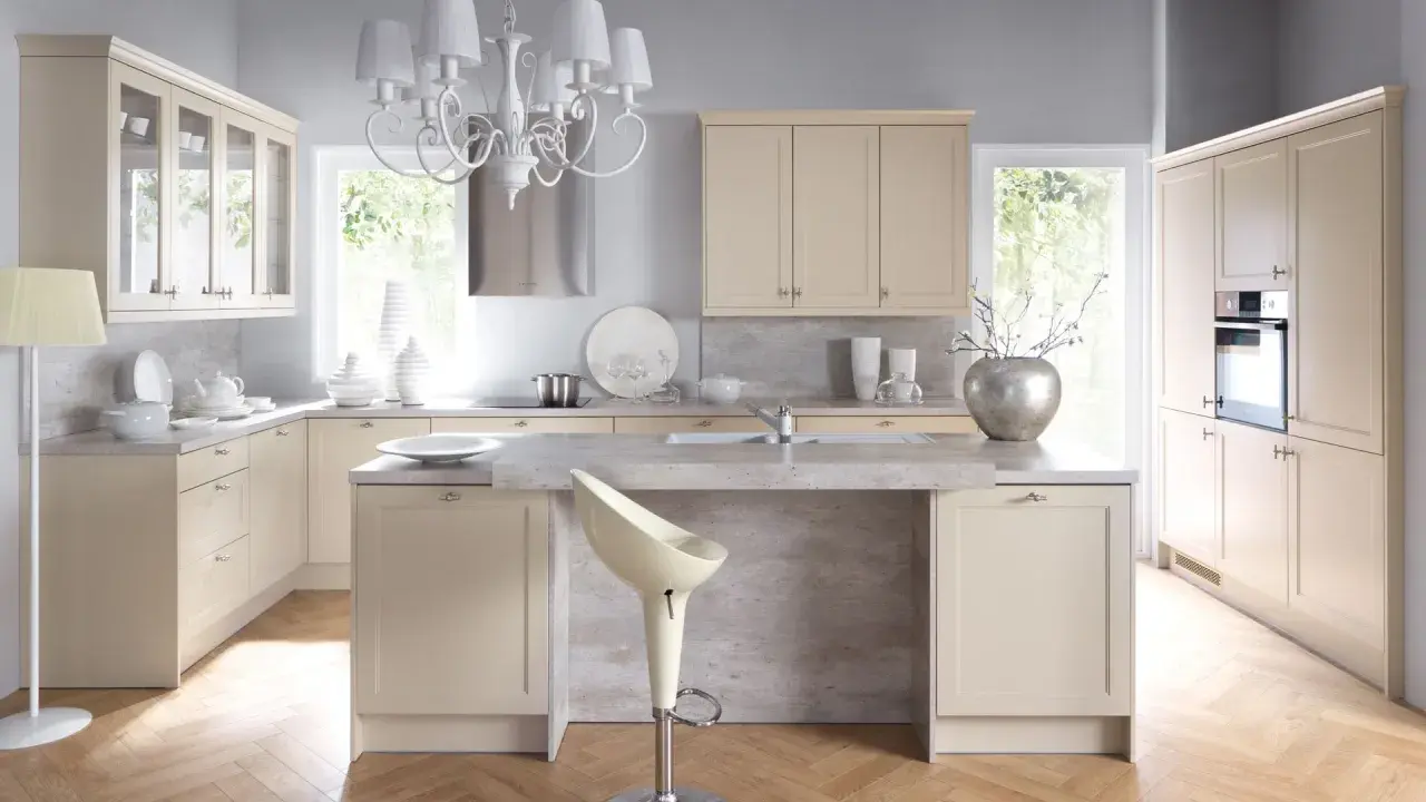 Jasna kuchnia w stylu shabby chic z kremowymi frontami, kamiennym blatem i ozdobnym żyrandolem.