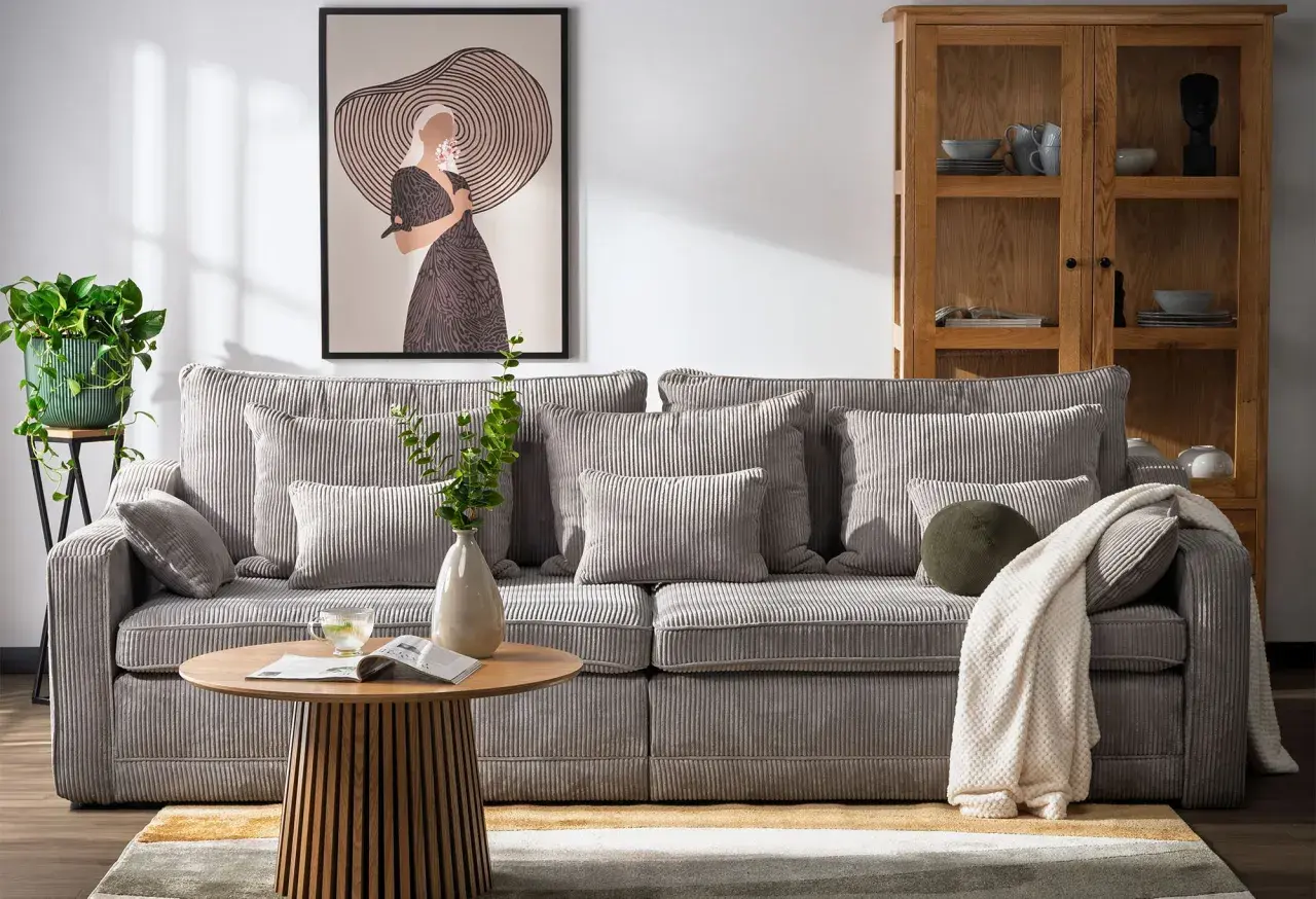 Miękka, sztruksowa kanapa a sofa w salonie, z poduszkami i kocem, obok stolika kawowego i obrazu.