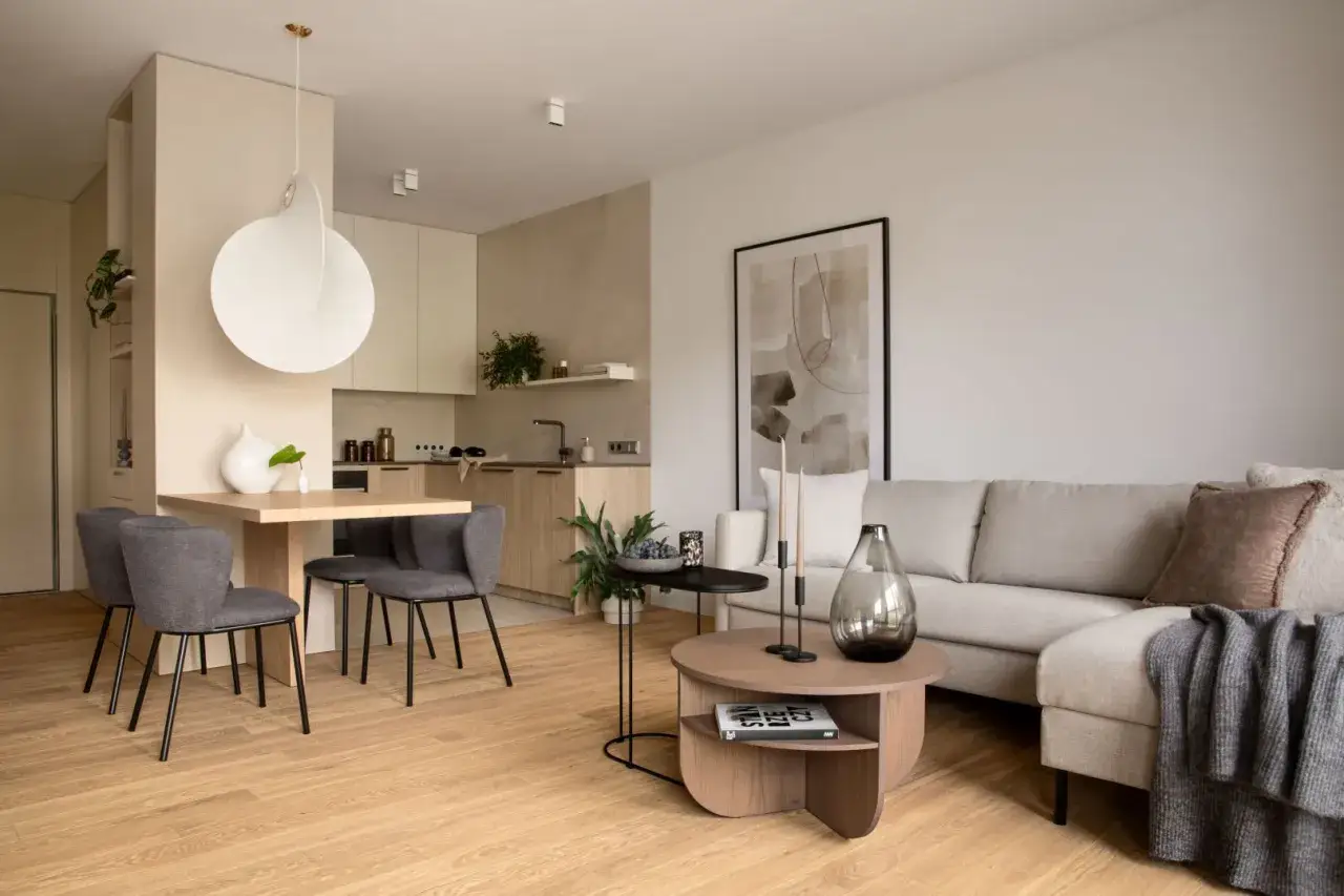 Przytulny salon inspiracje: jasna kanapa, drewniany stolik kawowy, nowoczesne krzesła przy stole i minimalistyczna kuchnia tworzą harmonijną przestrzeń.