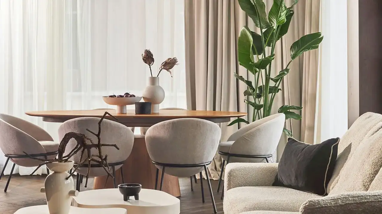 Eleganckie krzesła i sofa w neutralnych barwach, drewniany st&oacute;ł z dekoracjami. Inspiracja, jak łączyć kolory w mieszkaniu, by stworzyć harmonię.