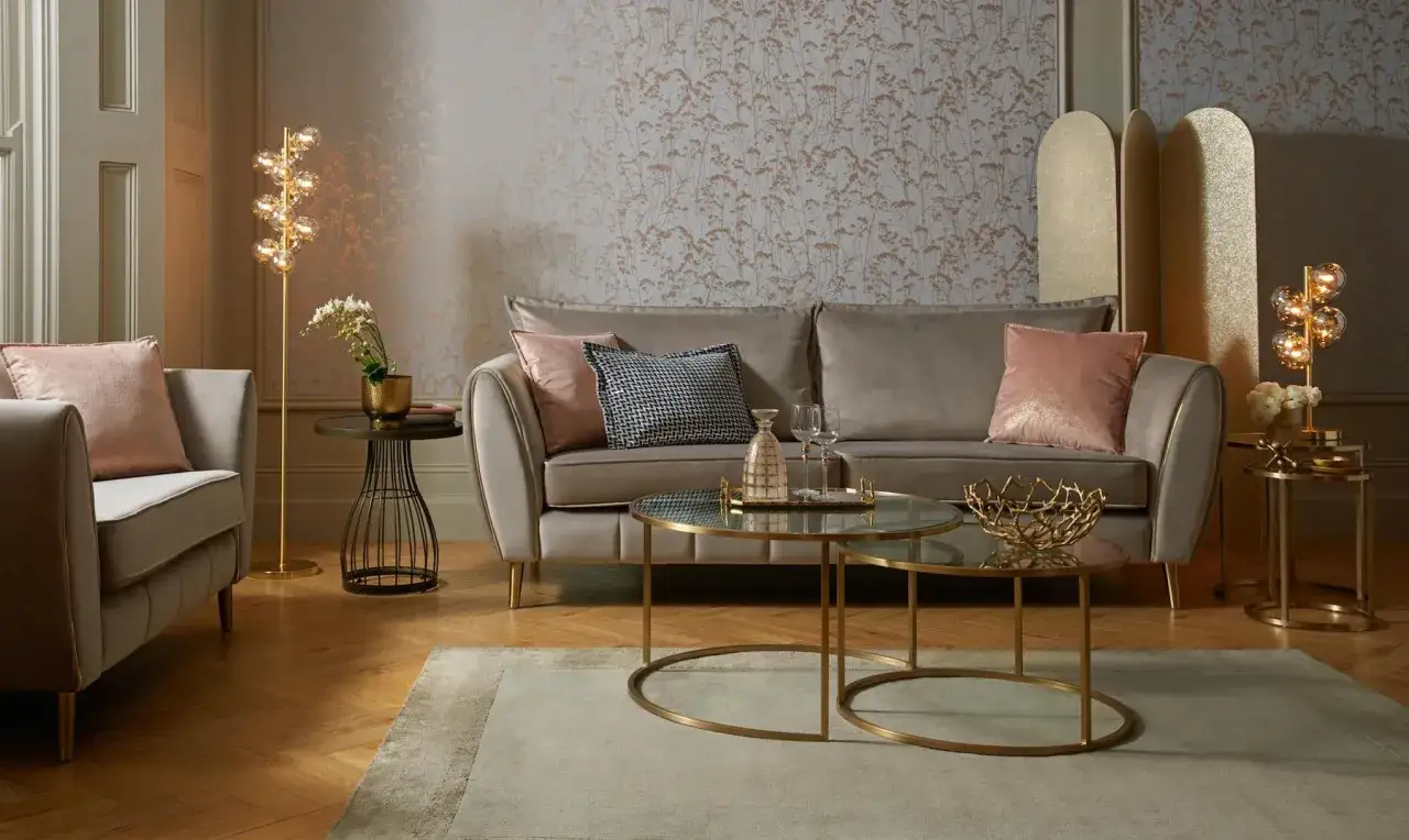 Przytulny salon glamour z beżową sofą, różowymi poduszkami i złotymi dodatkami.