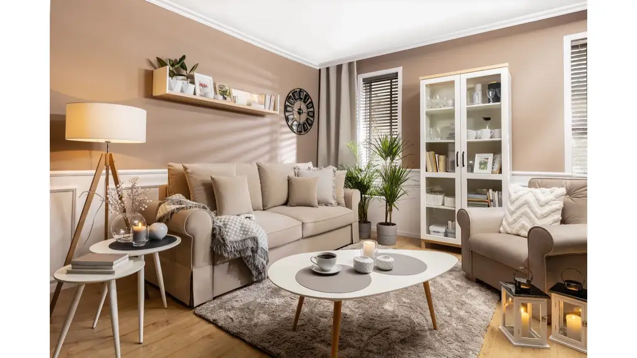 Przytulny salon w stylu boho z beżową kanapą, fotelem, stolikami kawowymi, regałem i dekoracjami.