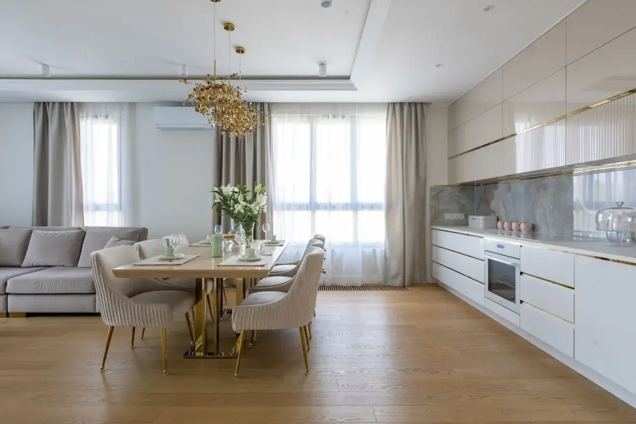 Elegancka kuchnia w stylu modern classic z jadalnią. Jasne meble, złote detale i designerska lampa tworzą luksusową atmosferę.