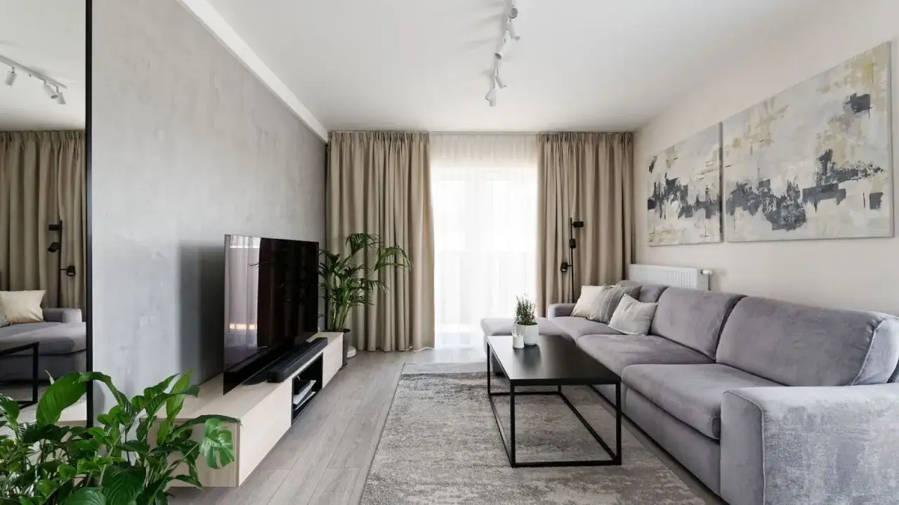 Nowoczesny salon z szarą kanapą i abstrakcyjnymi obrazami. Świetny pomysł na ścianę za kanapą &ndash; beton architektoniczny i dwie duże grafiki.