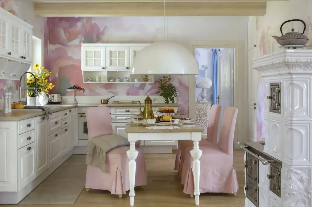 Urocza kuchnia w stylu shabby chic z pastelową tapetą, białymi meblami i różowymi obiciami krzeseł.