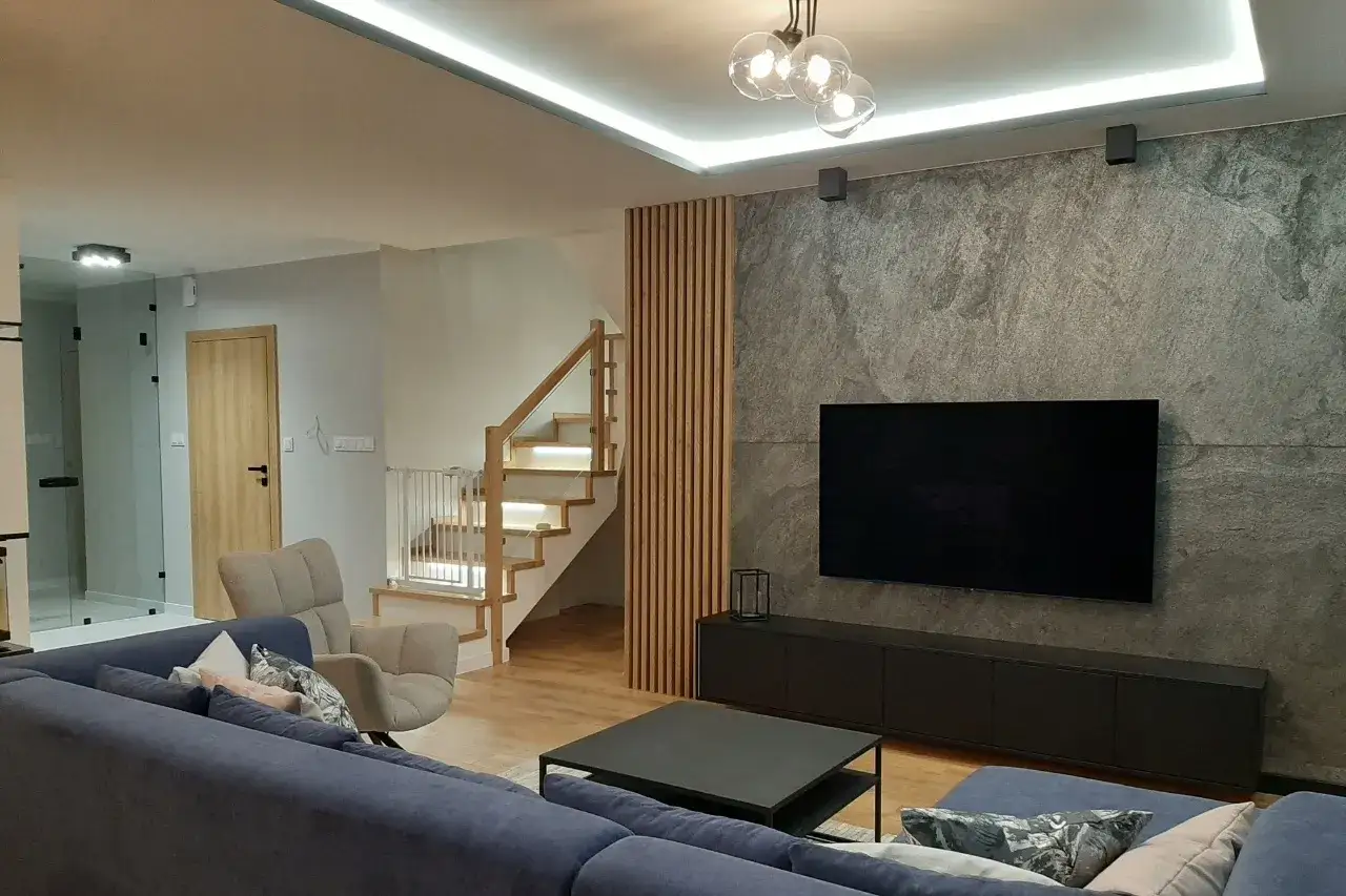 Nowoczesne lamele w salonie aranżacje tworzą przytulną atmosferę przy schodach. Szara ściana z TV i wygodna kanapa dopełniają wnętrze.